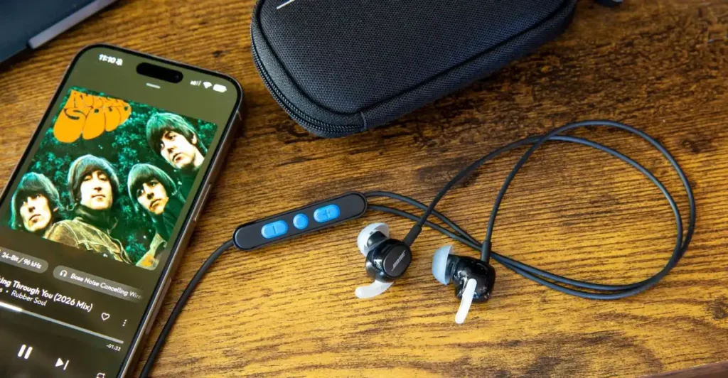 Bose Noise Cancelling Wired Earbuds terhubung ke ponsel pintar memutar musik audio resolusi tinggi di atas meja kayu